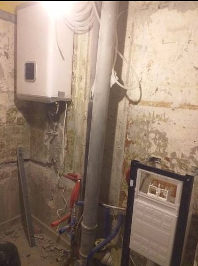 Montaż podtynkowego zestawu WC w surowej łazience z widocznym bojlerem i rurami kanalizacyjnymi przed wykończeniem ścian.