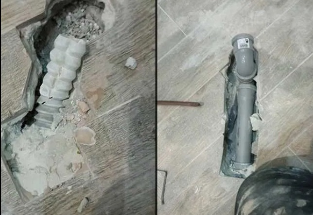 Odkryta instalacja kanalizacyjna w podłodze z imitacji drewna, z widocznymi elementami rur i uszkodzeniami płytek w trakcie prac.