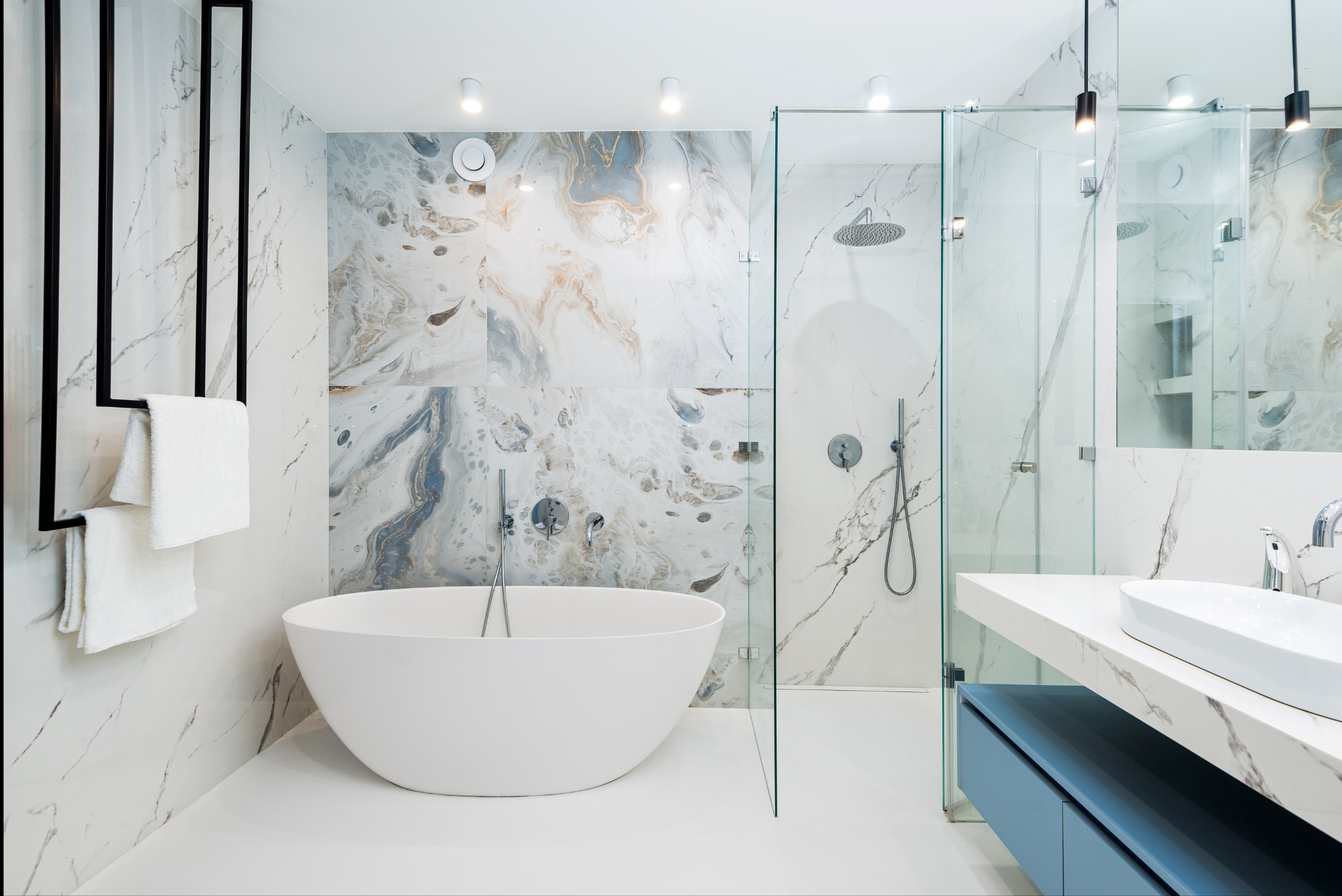 Nowoczesna łazienka w Gliwicach z wolnostojącą białą wanną, kabiną prysznicową ze szklanymi ścianami i umywalką nablatową na blacie z szafką w kolorze błękitnym, całość w jasnej kolorystyce...