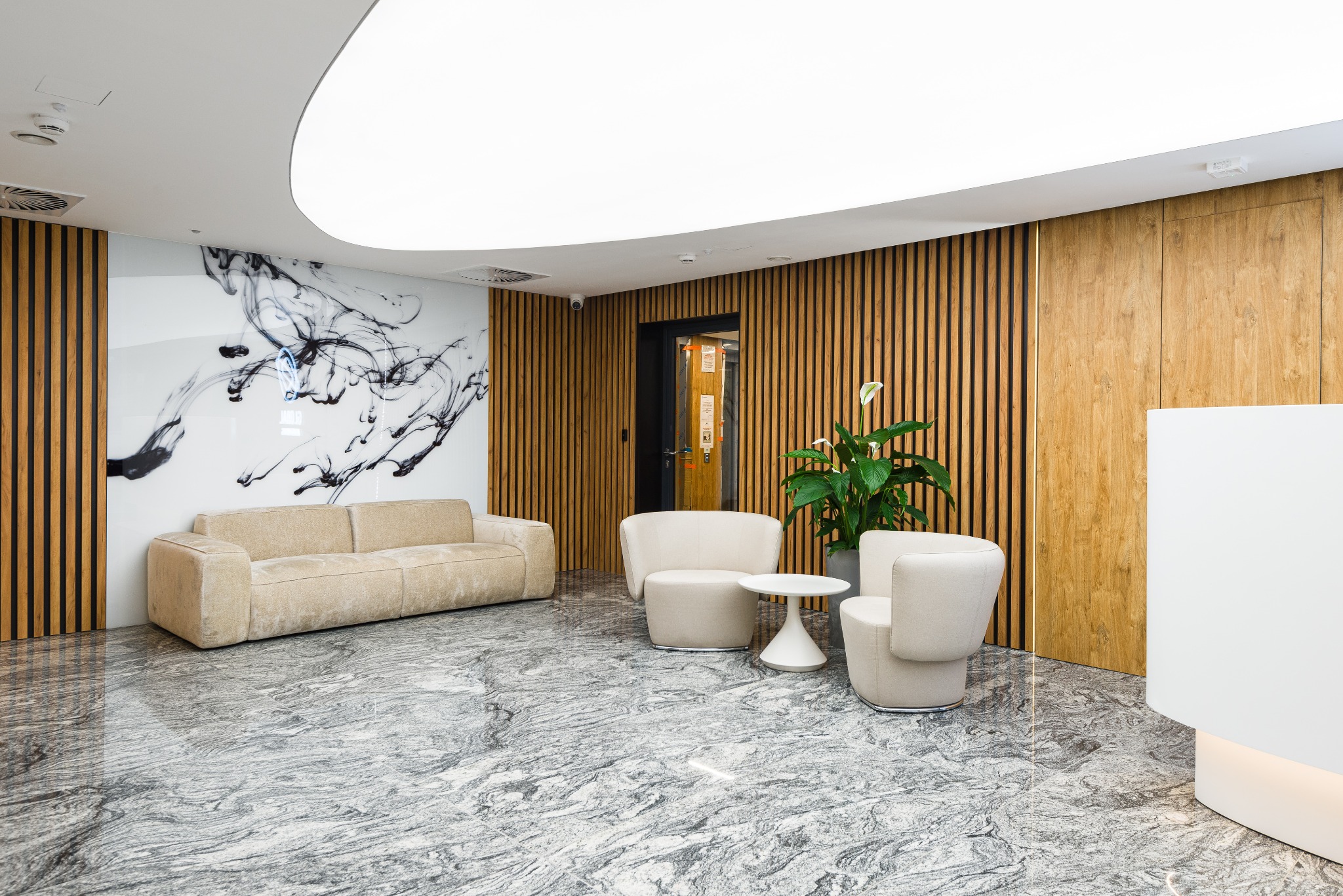 Eleganckie wnętrze biurowe z sofą, fotelami i marmurową podłogą. Ściana z drewnianymi panelami i abstrakcyjną grafiką. Nowoczesny design z rośliną doniczkową.