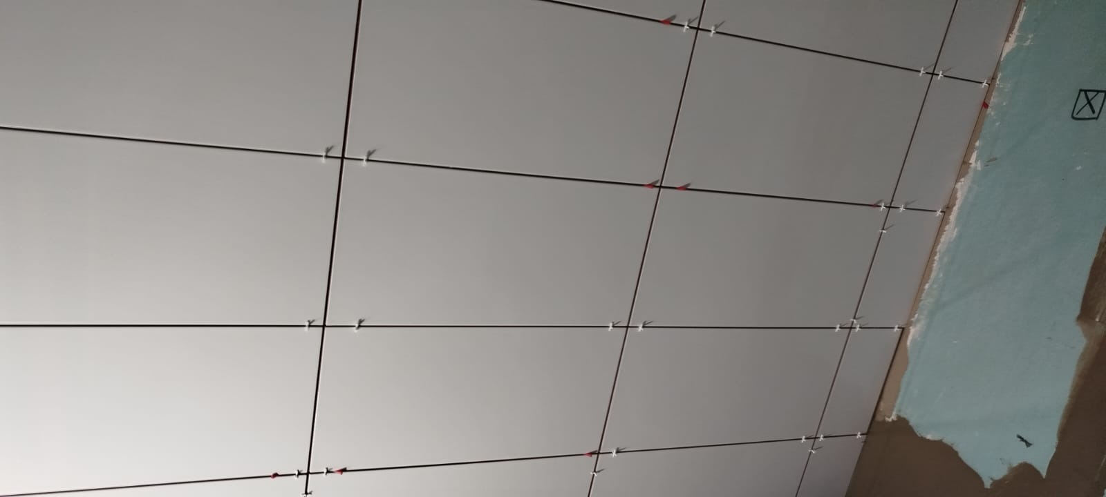 Świeżo ułożone, jasnoszare płytki ścienne z krzyżykami dystansowymi, widoczny fragment surowej ściany z zaznaczonymi liniami.