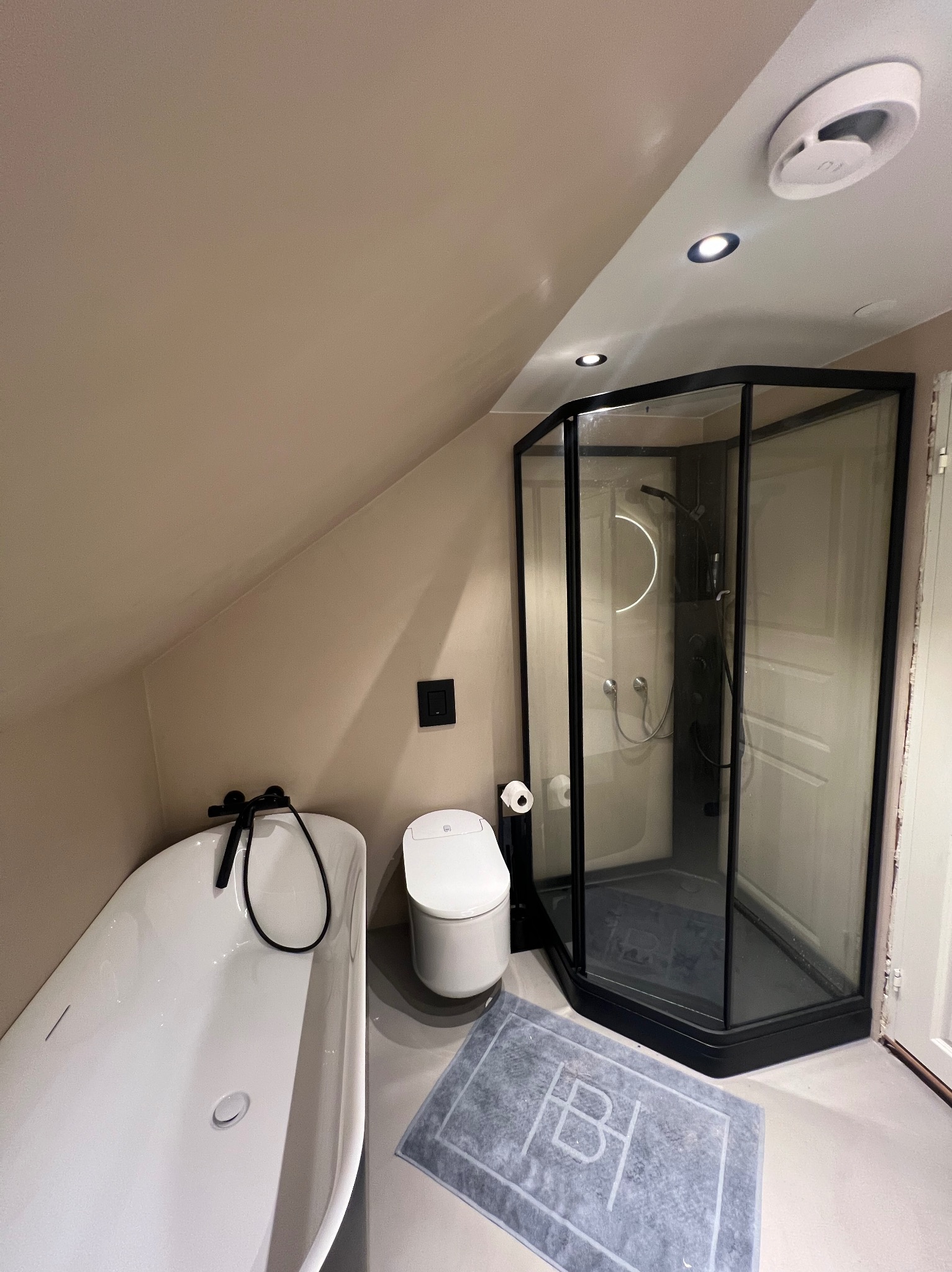 Nowoczesna łazienka na poddaszu w Niemcach z białą wanną wolnostojącą, toaletą i kabiną prysznicową z czarnymi ramami, oświetlona punktowo.