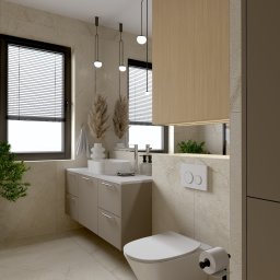 Karolina Szczesna Wnętrza - Jasna łazienka z beżowymi płytkami, wisząca szafka z umywalką nablatową, toaleta wisząca, dwie ciemne okna z żaluzjami, dekoracyjne trawy w wazonach i zielona roślina doniczkowa.