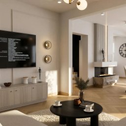 Karolina Szczesna Wnętrza - Nowoczesny salon z jasną podłogą w jodełkę, białymi ścianami z subtelnymi panelami, dużym TV, okrągłymi kinkietami, bio-kominkiem z kamienną podstawą i złotym żyrandolem z kulistymi kloszami.