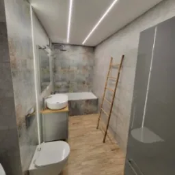 Nowoczesna łazienka z szarą mozaiką, podwieszaną toaletą, umywalką nablatową na szafce z drewnianym blatem, bambusową drabinką i podświetleniem LED na suficie i ścianie.