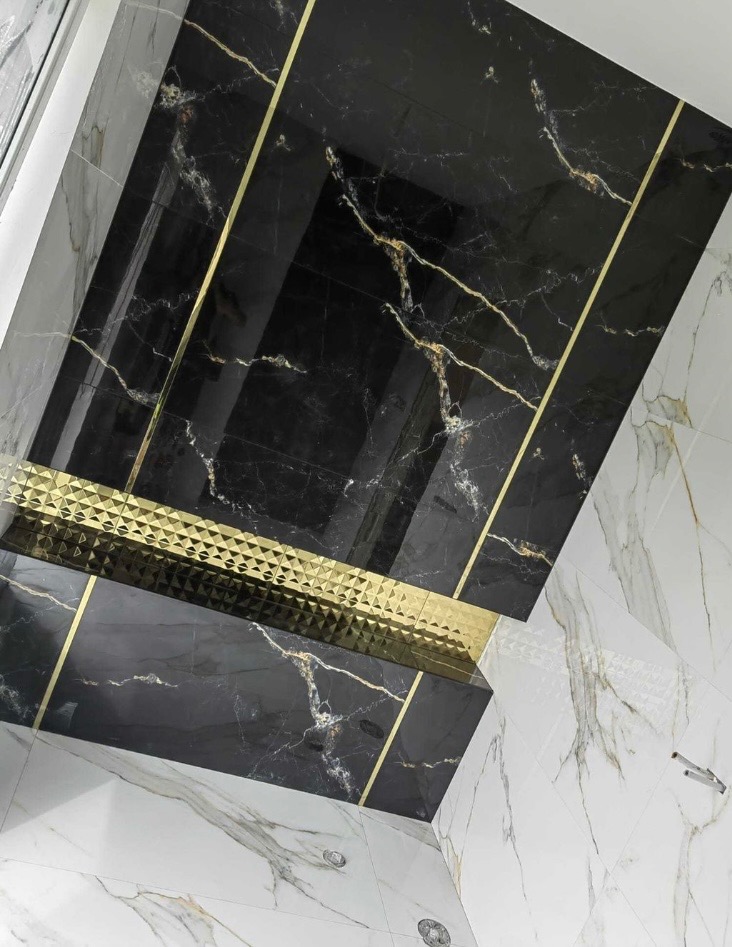 Wykończona łazienka z czarnymi płytkami imitującymi marmur z złotymi żyłami i złotymi listwami dekoracyjnymi, połączona z białymi płytkami marmurowymi na ścianie i podłodze.
