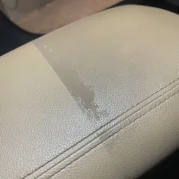 Fragment jasnej, skórzanej tapicerki samochodowej, widoczna różnica w czystości po praniu na fragmencie powierzchni.