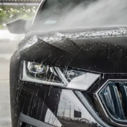 Czarny samochód osobowy marki Skoda podczas mycia, widoczne krople wody na karoserii i reflektorze.