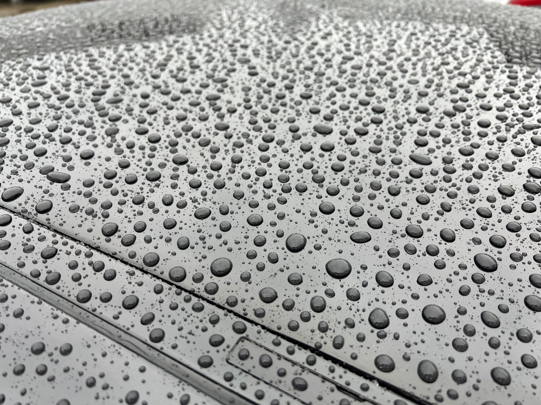 Błyszcząca, czarna karoseria samochodu pokryta kroplami wody po deszczu, widoczne detale lakieru i odbicia światła.