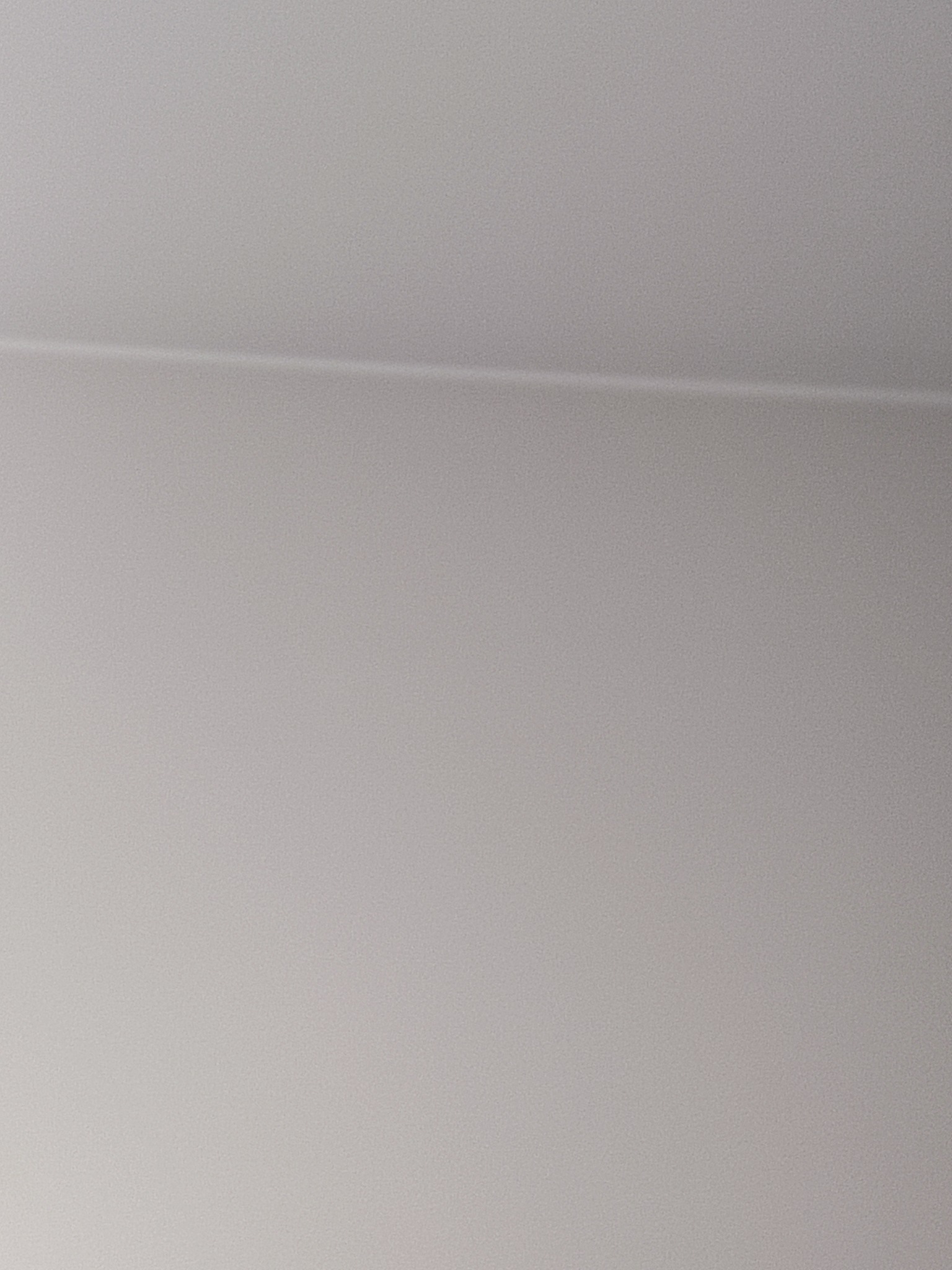 Fragment białego sufitu z widoczną linią łączenia płyt, oświetlonego delikatnym, rozproszonym światłem.