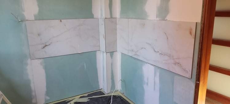 Płytki imitujące marmur ułożone na ścianie w rogu łazienki, widoczne ślady po gładzi szpachlowej na ścianach i podłodze zabezpieczonej folią.