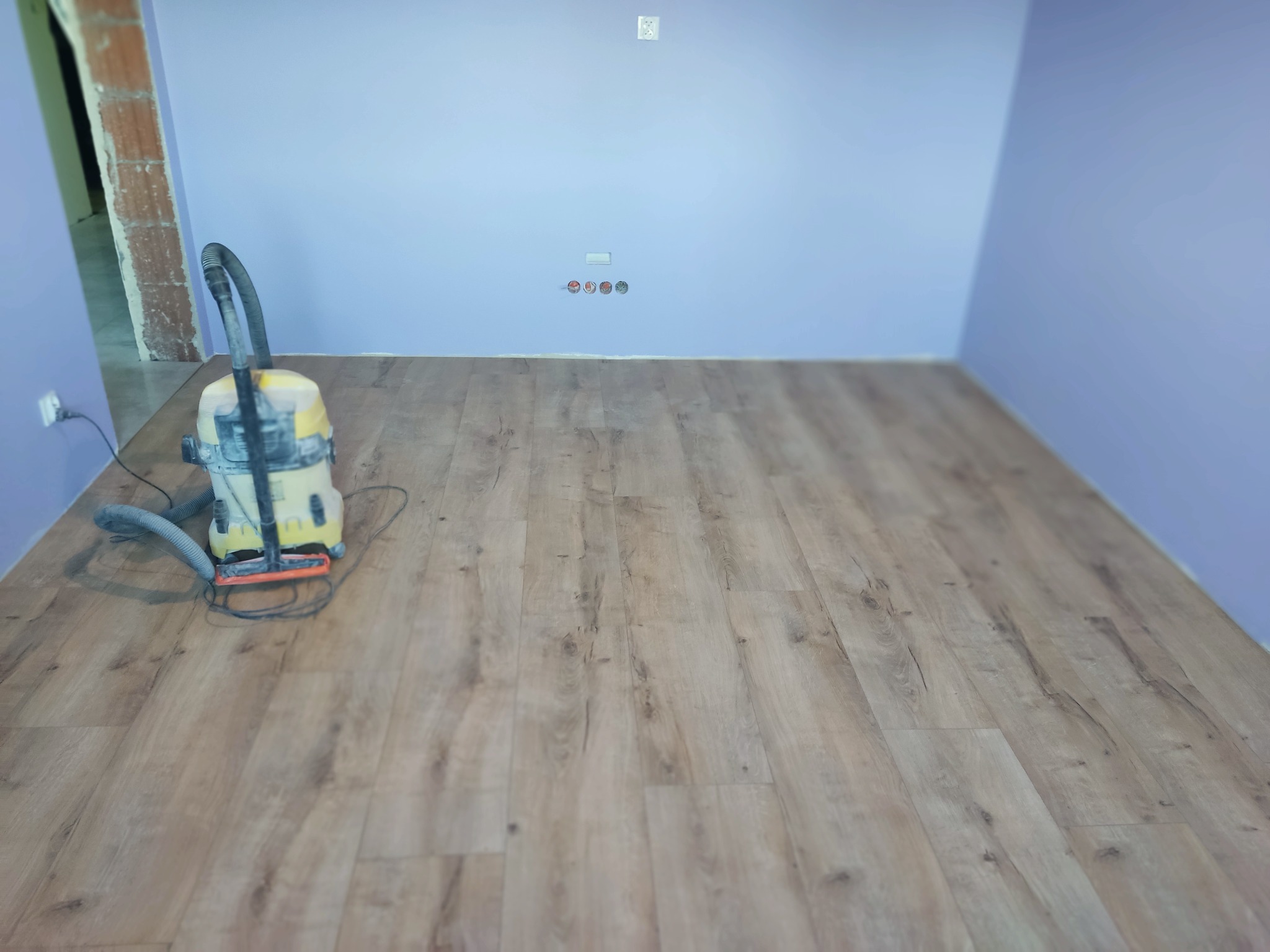 Pokój po pracach wykończeniowych z nową podłogą laminowaną i świeżo pomalowanymi ścianami na fioletowo, widoczny odkurzacz przemysłowy.