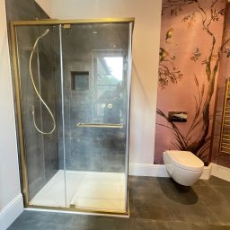 Łazienka i Dom Melchior Nowociński - Stylowa łazienka z kabiną prysznicową w złotej ramie, grafitowymi płytkami, toaletą i tapetą w kwiaty i ptaki. Nowoczesny design z dbałością o detale.