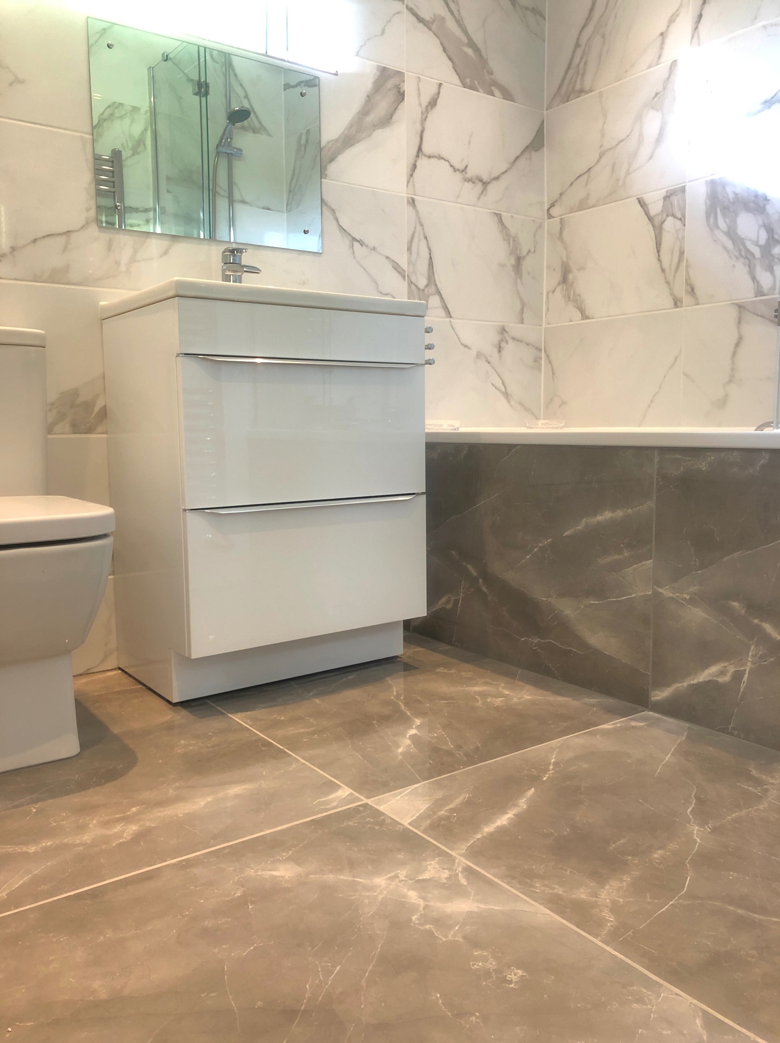 Ukończona łazienka z marmurowymi płytkami w odcieniach szarości i bieli. Widoczna toaleta, umywalka z szafką i fragment wanny.