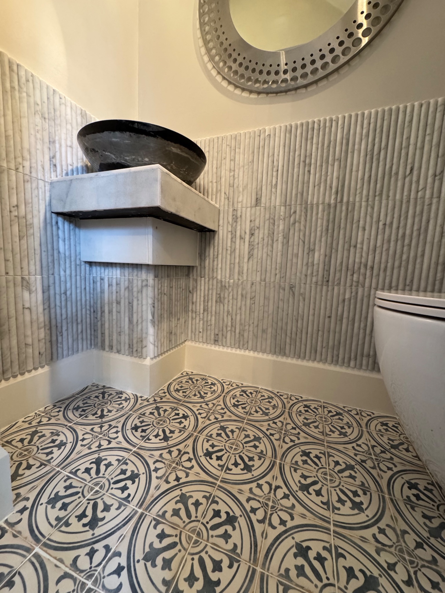 Nowoczesna łazienka z marmurowymi płytkami ściennymi, wzorzystą posadzką i oryginalną umywalką w kształcie misy na marmurowym blacie.