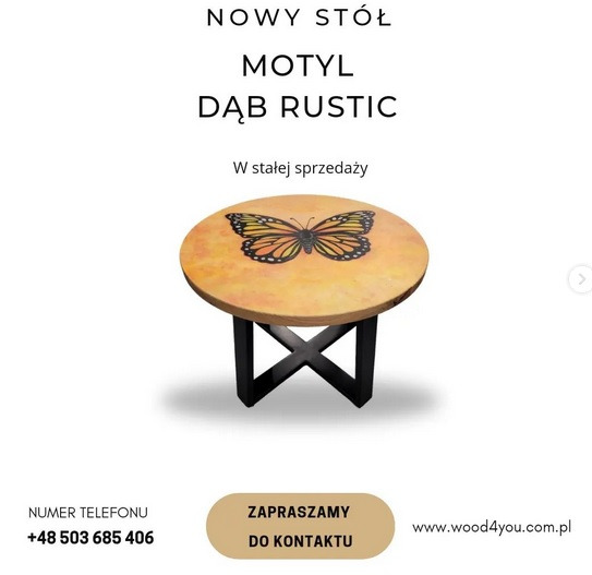 Okrągły stolik kawowy z blatem z motywem motyla na tle imitującym dąb rustykalny, wsparty na czarnych, krzyżujących się nogach. Produkt reklamowany jako 'Nowy Stół Motyl Dąb Rustic'.