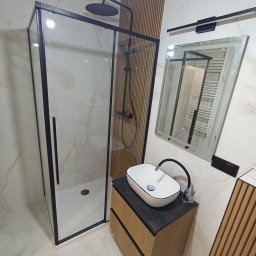 VOLODYMYR ZHURAVEL - Nowoczesna łazienka z kabiną prysznicową z czarnymi ramami, umywalką nablatową na szafce z drewnianymi lamelami i lustrem z podświetleniem LED.