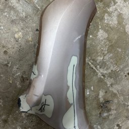 PMD-Design Sp. z o.o. - Element karoserii samochodowej w trakcie naprawy blacharskiej, z widocznymi szpachlami i zaznaczeniami, leżący na betonowej posadzce.