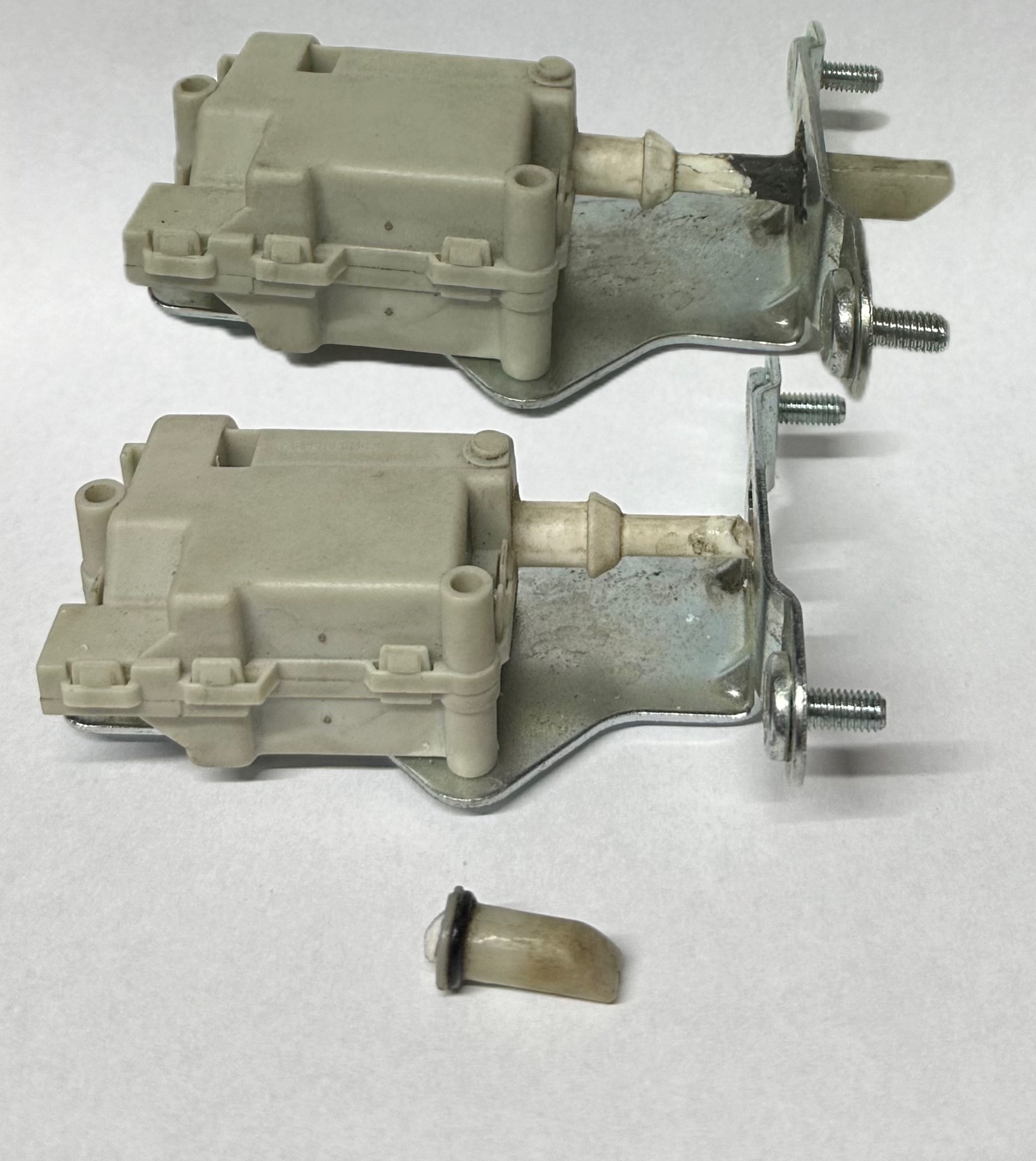 Dwa elektrozamki do bramy z metalowymi uchwytami i śrubami, jeden element zamka leży oddzielnie na białym tle.