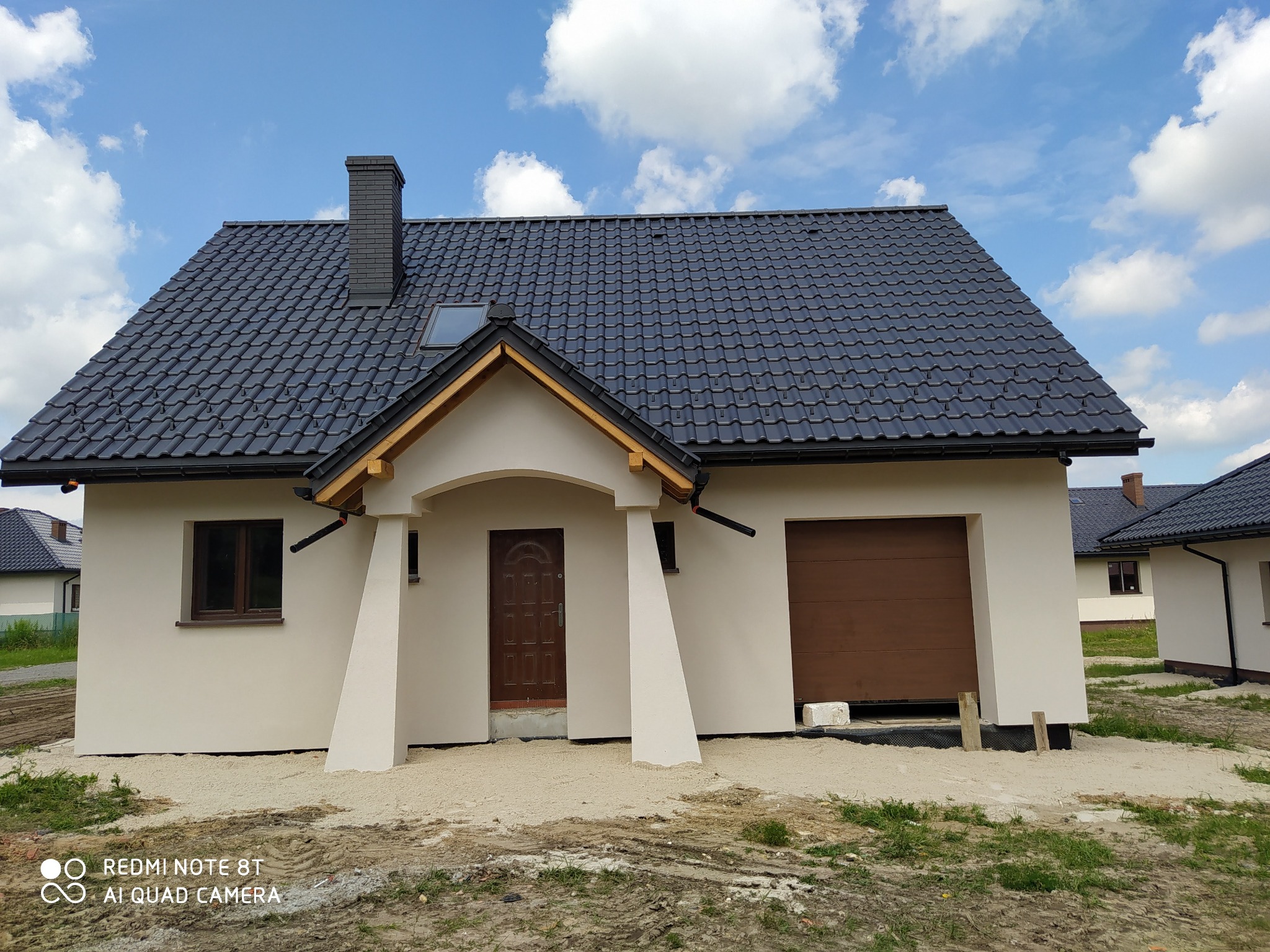 Nowo wybudowany, parterowy dom z ciemną dachówką i kominem z cegły, jeszcze bez zagospodarowanego terenu wokół.