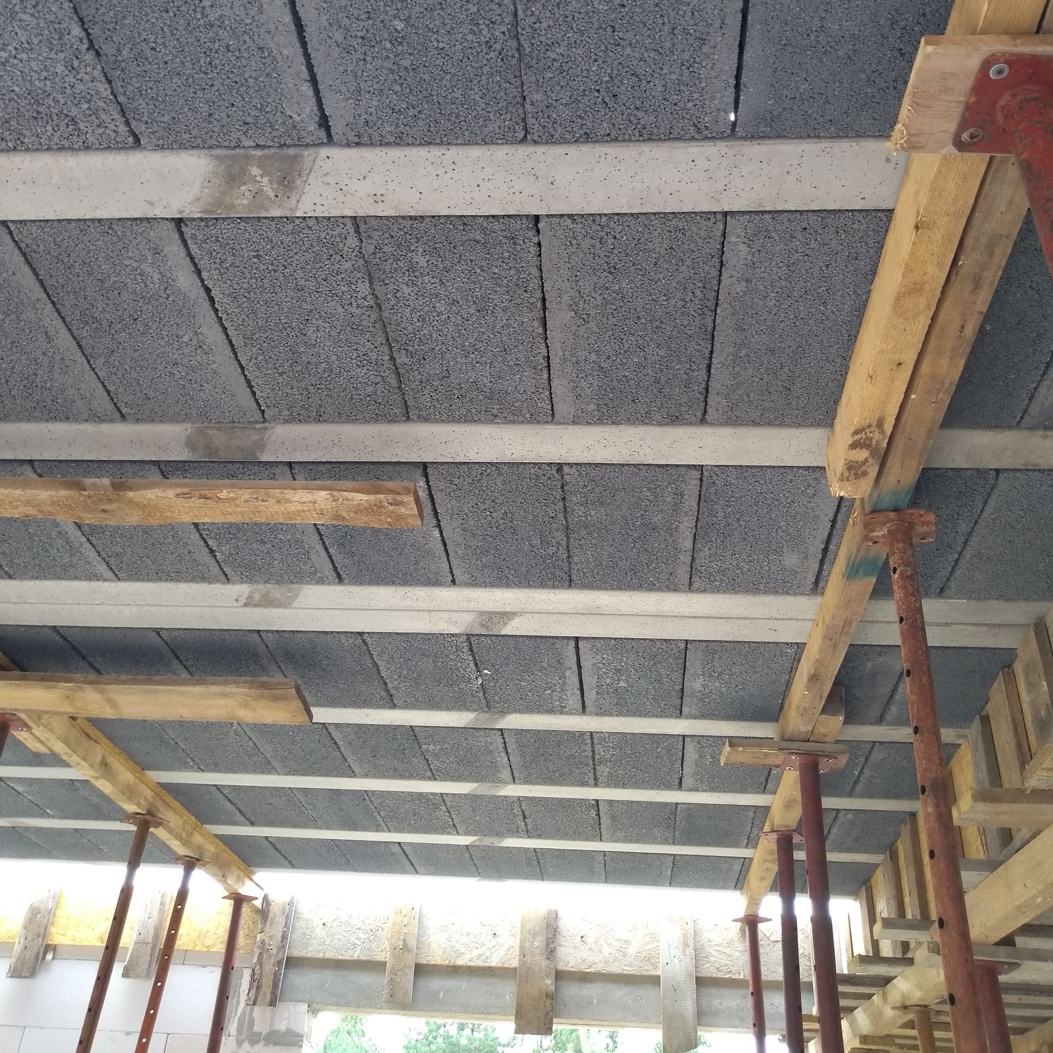 Strop z szarego betonu komórkowego z widocznymi belkami nośnymi i podporami stalowymi podczas budowy.