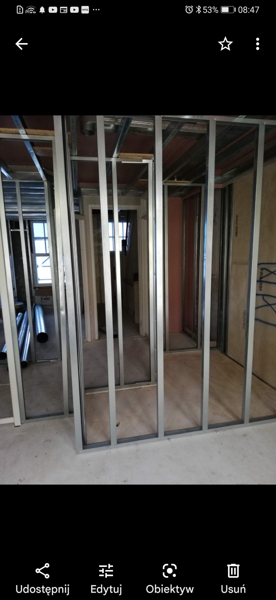 Konstrukcja ścian działowych z profili stalowych na podłodze w trakcie budowy, widoczne rury wentylacyjne i okno w tle.