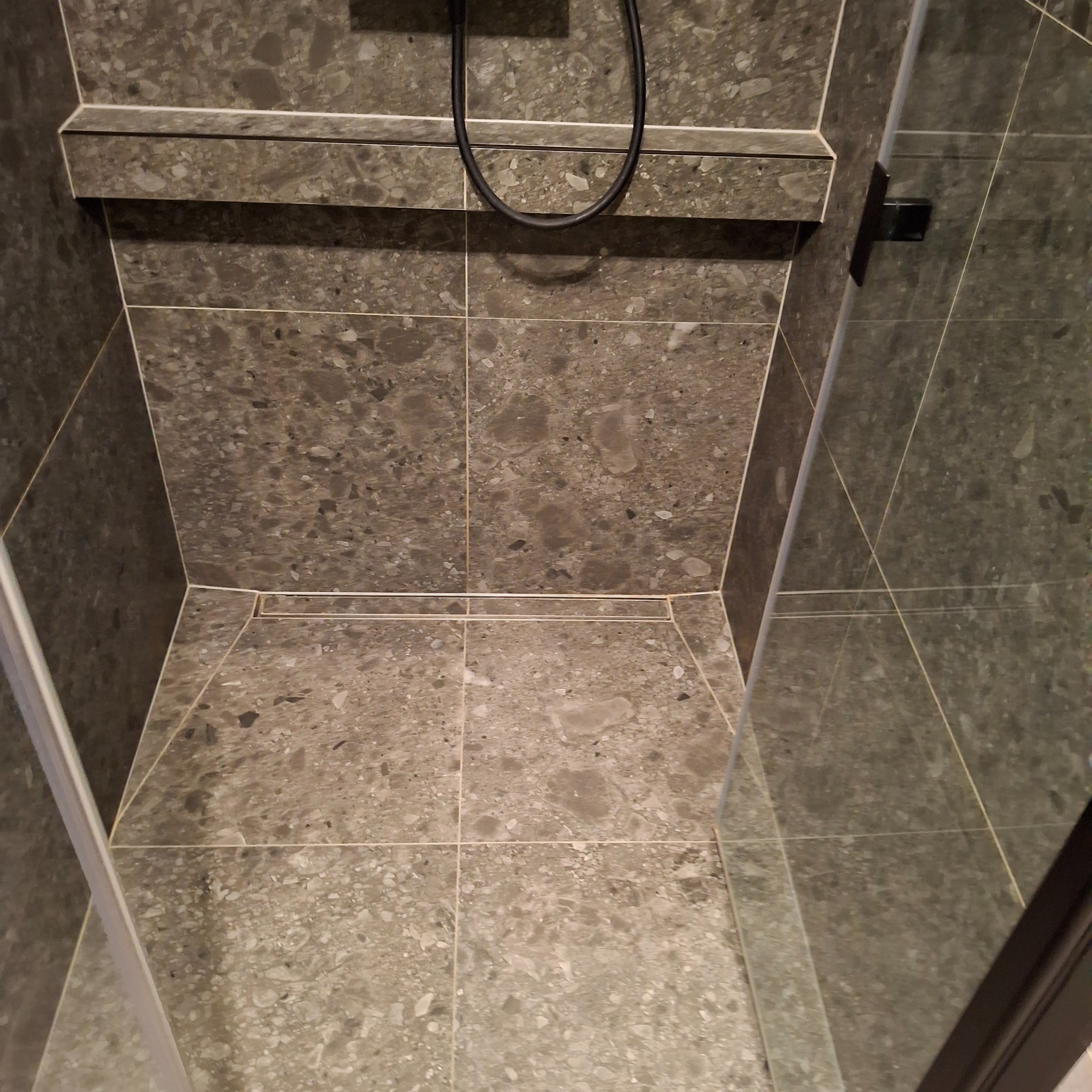 Nowoczesna kabina prysznicowa z szarymi płytkami imitującymi kamień, z odpływem liniowym i czarną armaturą.