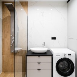 ALEKSANDRA BORAWSKA - Nowoczesna łazienka z kabiną prysznicową typu walk-in, umywalką nablatową na szafce z szufladami i pralką. Białe marmurowe płytki i drewniane akcenty.