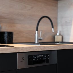 ALEKSANDRA BORAWSKA - Minimalistyczna kuchnia: czarne szafki, drewniany blat, metalowa bateria i akcesoria. Widoczny panel sterowania zmywarki Electrolux.