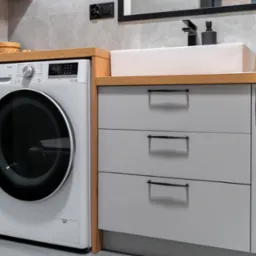 Nowoczesna łazienka z szarą zabudową meblową, pralką LG i umywalką nablatową. Drewniany blat, czarne uchwyty i armatura. Minimalistyczny design z szarymi płytkami.