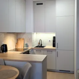 Nowoczesna kuchnia w odcieniach szarości z drewnianym blatem, czarnymi akcentami i oświetleniem punktowym. Widoczny stół z krzesłami.