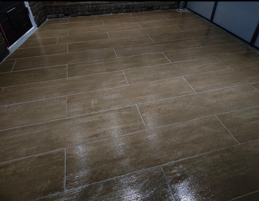 Ułożona podłużna terakota imitująca drewno na patio, widoczne fugi i mokra powierzchnia po czyszczeniu.