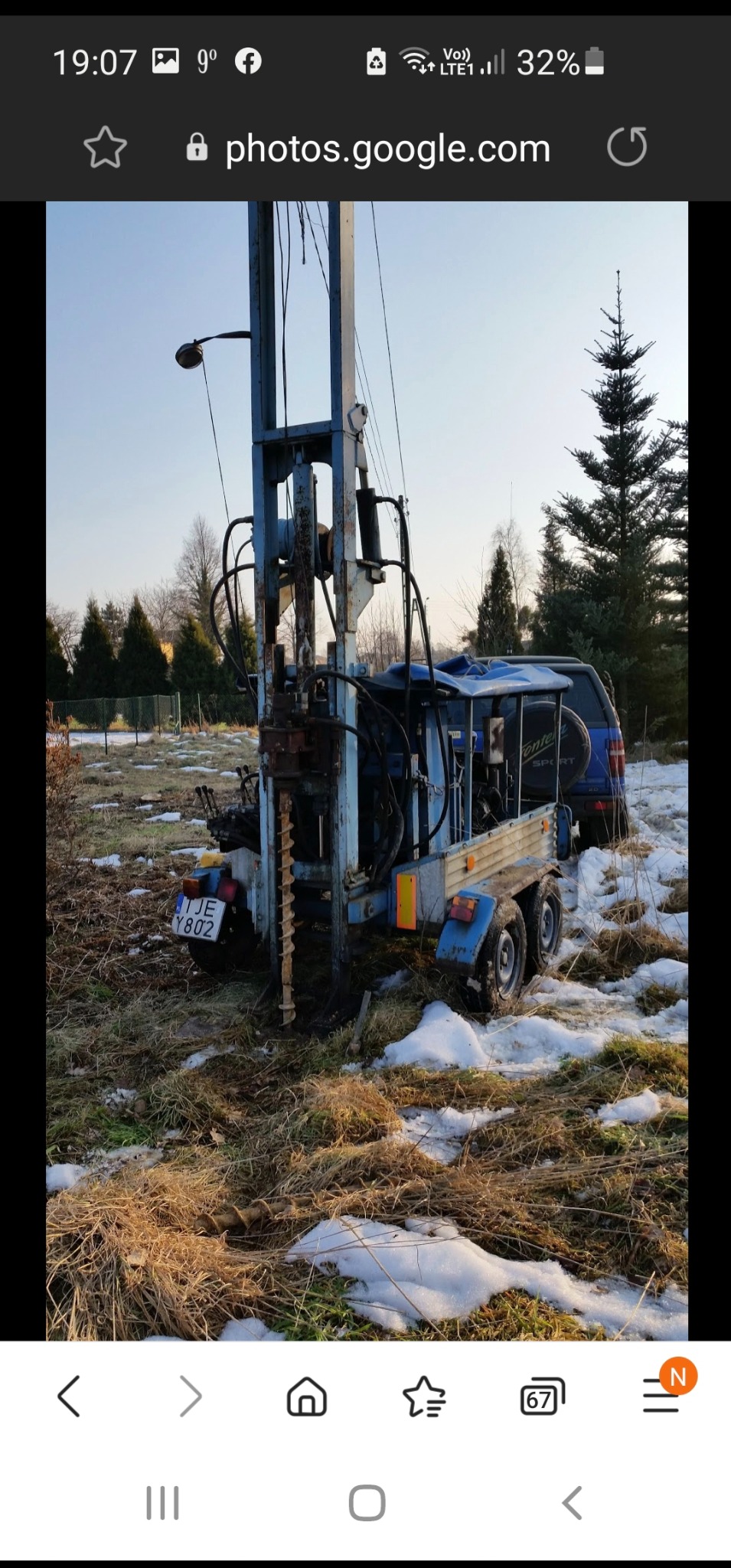 Mobilna wiertnica z wiertłem świdrowym, zaparkowana na trawiastym terenie z resztkami śniegu, obok zaparkowany samochód terenowy, widoczne tablice rejestracyjne pojazdów.