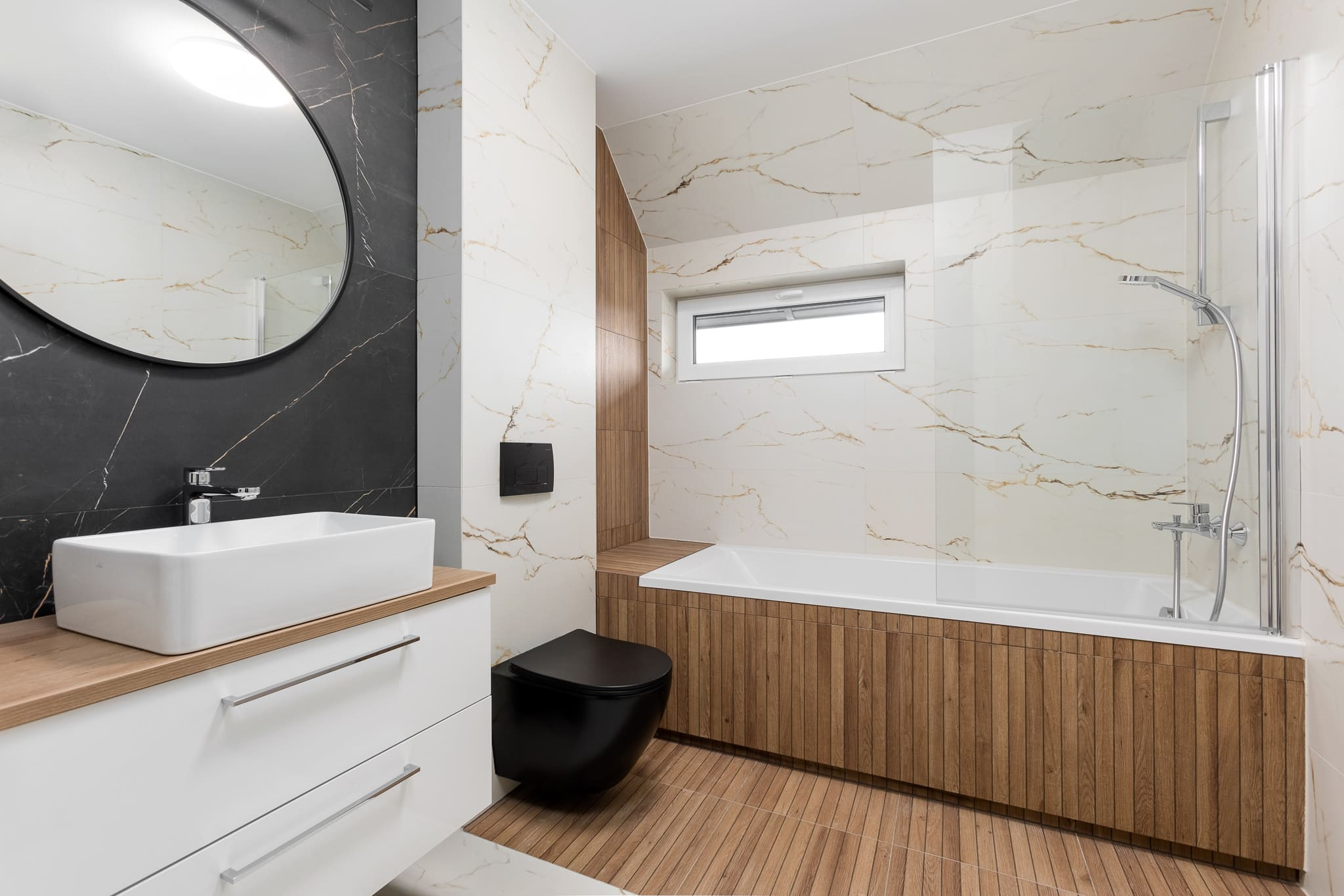 Nowoczesna łazienka z czarną armaturą, białymi szafkami i wanną obudowaną drewnopodobnymi panelami, oświetlona naturalnym światłem z okna.