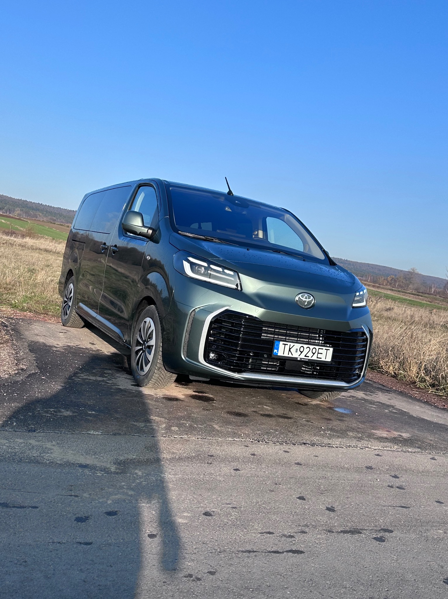 Zielony, nowoczesny bus na drodze w Napękowie, z polską tablicą rejestracyjną, sfotografowany w słoneczny dzień na tle pól i wzgórz.