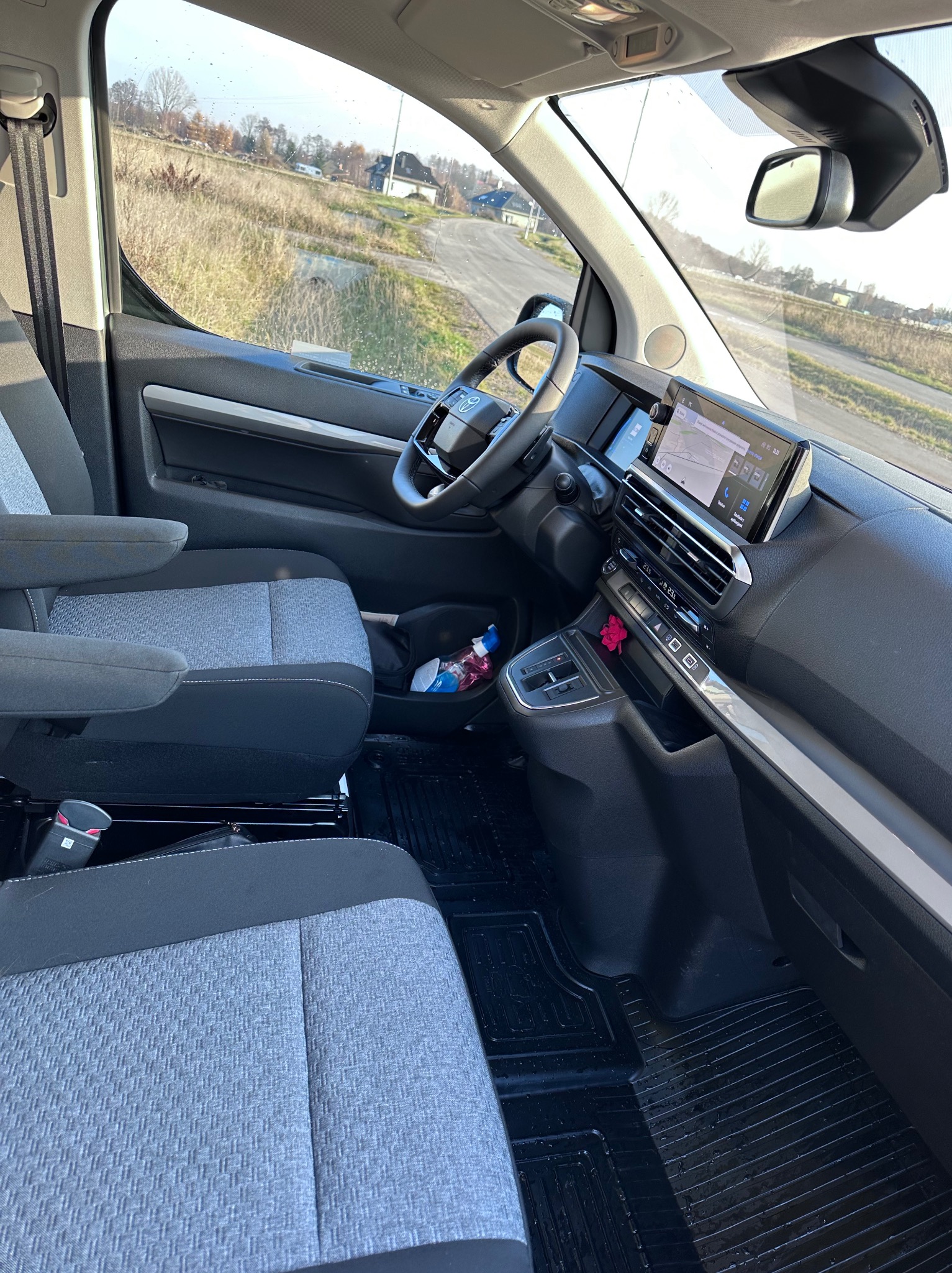 Wnętrze nowoczesnego busa z widocznymi fotelami pasażerskimi, deską rozdzielczą z nawigacją GPS i widokiem na drogę za oknem.