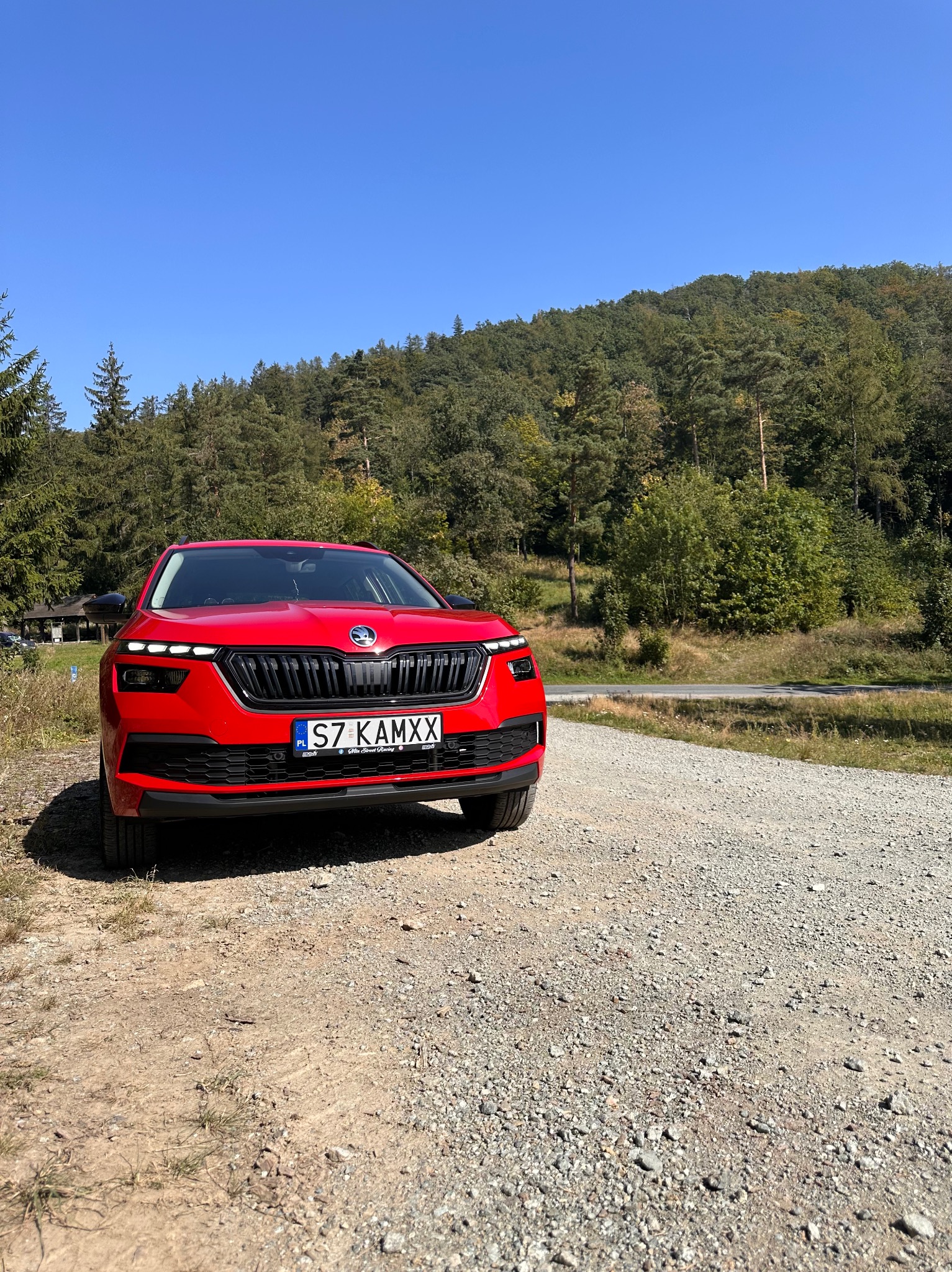 Czerwona Skoda Kamiq zaparkowana na szutrowej drodze z lasem w tle, widok z przodu.