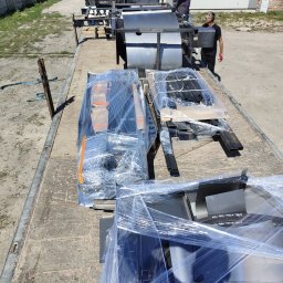 TS WELD TOMASZ SMYTRY - Transport elementów konstrukcji stalowej na platformie ciężarówki, pracownicy w tle, elementy zabezpieczone folią stretch.