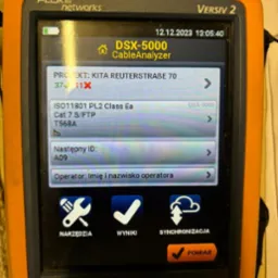 Pomarańczowy tester kabli Fluke Networks Versiv 2 DSX-5000 CableAnalyzer wyświetlający wyniki pomiaru okablowania strukturalnego, w tym informacje o projekcie, standardzie ISO11801, kategorii Cat 7...