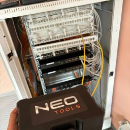 SOLO Dawid Solczak - Szafa rack z patch panelem, switchem i okablowaniem, widziana z perspektywy osoby trzymającej skrzynkę narzędziową Neo Tools.