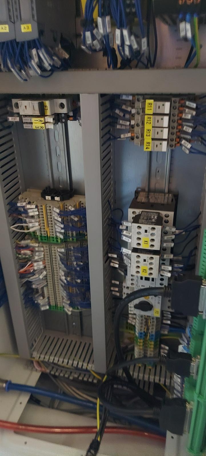 Wnętrze szafy sterowniczej z widocznymi elementami automatyki, przewodami i złączkami oznaczonymi etykietami, prezentujące skomplikowaną sieć połączeń elektrycznych.