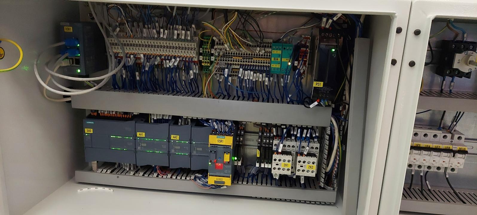 Wnętrze szafy sterowniczej z modułami Siemens, przewodami i listwami zaciskowymi, widoczne diody sygnalizacyjne i oznaczenia na elementach.