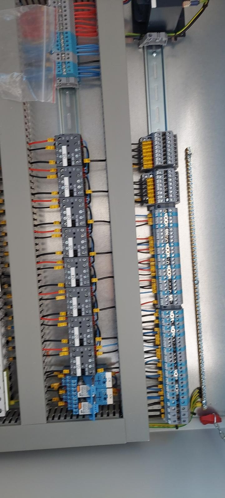 Wnętrze szafy sterowniczej z widocznymi listwami zaciskowymi, przewodami o różnych kolorach i zabezpieczeniami, uporządkowane w szarym panelu.