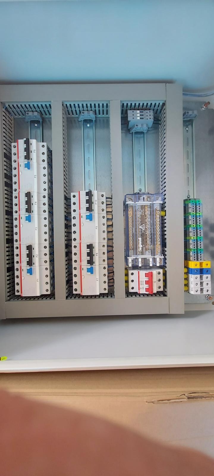 Rozdzielnica elektryczna z trzema rzędami bezpieczników, widoczne szyny DIN i złącza, zamontowana w szarej obudowie wewnątrz budynku.