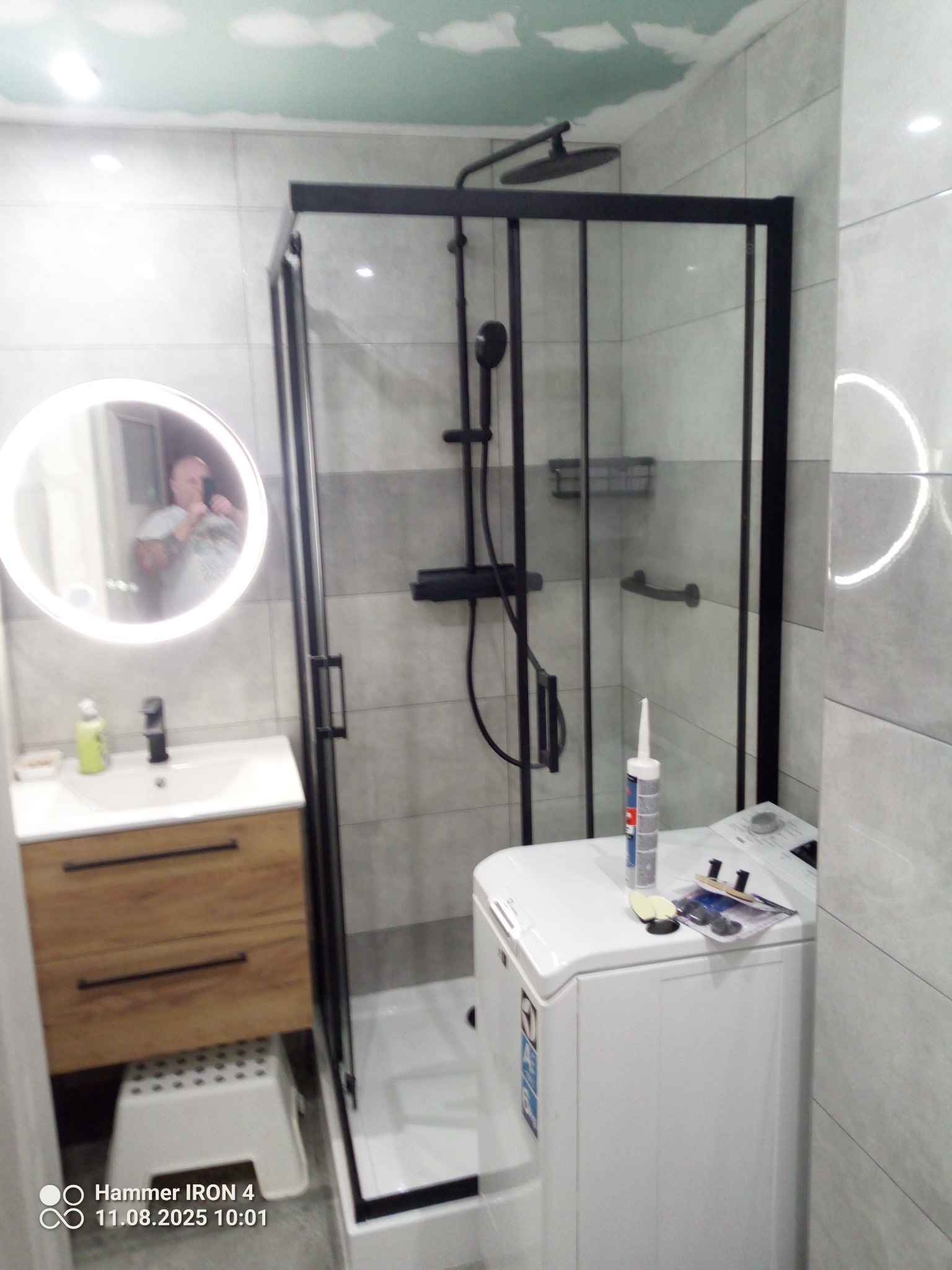 Wykończona łazienka w Gnojniku z kabiną prysznicową typu walk-in z czarnymi profilami, umywalką z szafką i okrągłym lustrem z podświetleniem LED.