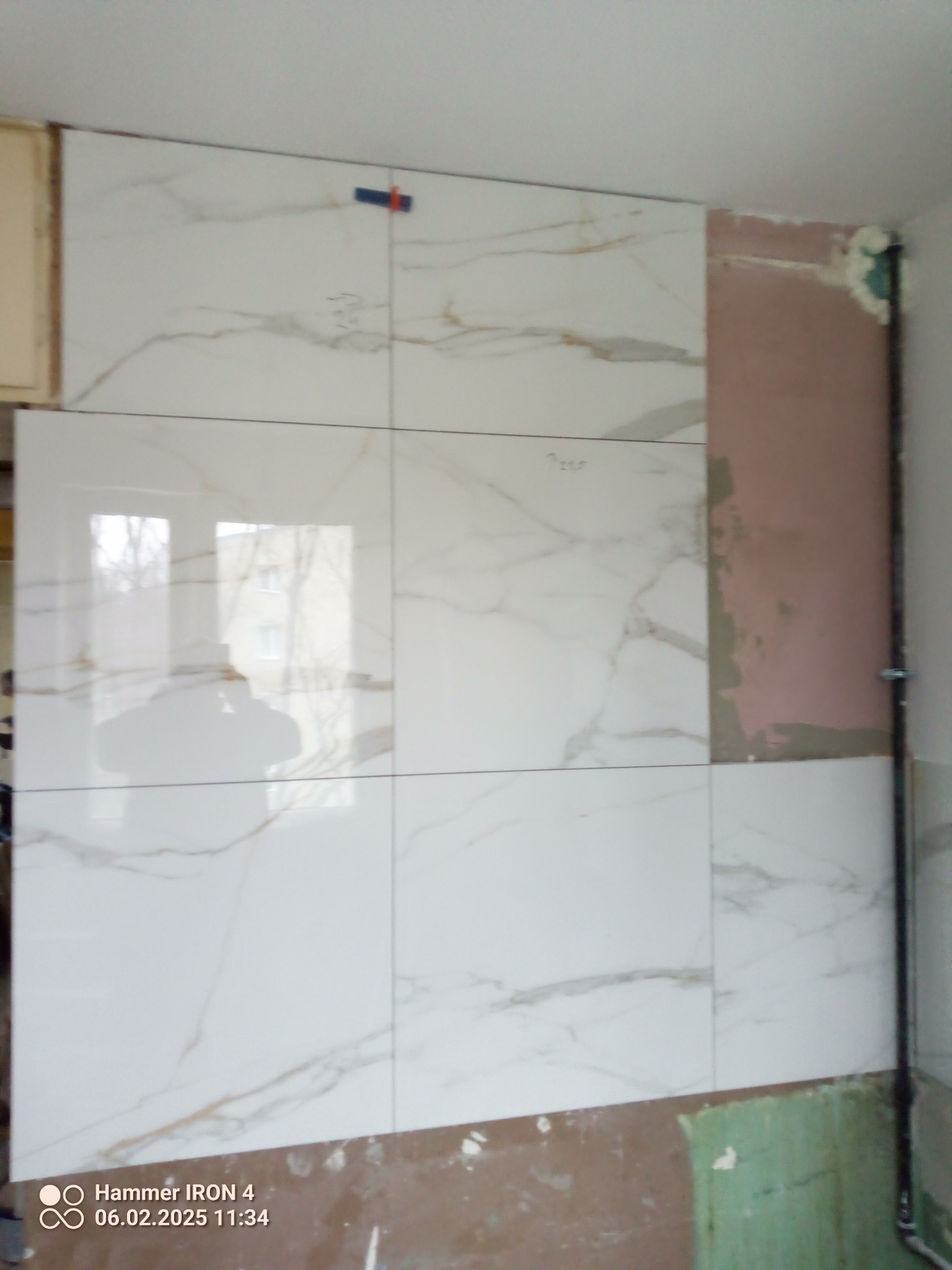 Układanie białych płytek imitujących marmur na ścianie w trakcie remontu łazienki. Widoczne fragmenty nieotynkowanej ściany i narzędzia glazurnicze.