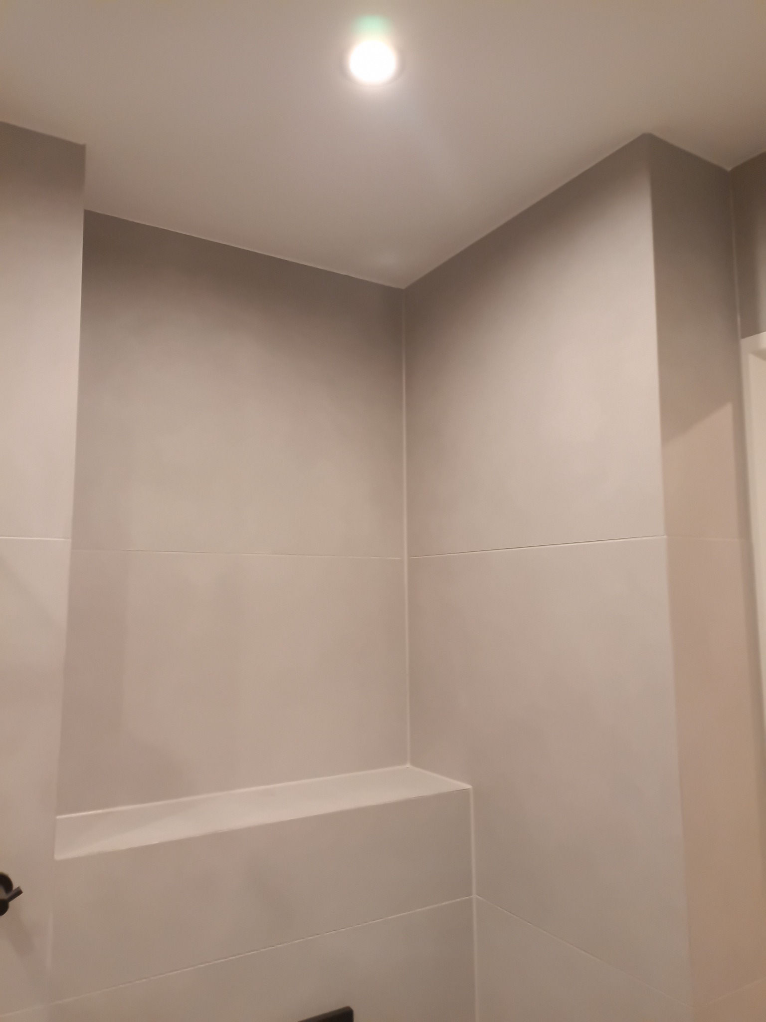 Minimalistyczna, jasna łazienka z półką wnękową wyłożoną płytkami. Punktowe oświetlenie sufitowe. Czyste linie i neutralna kolorystyka tworzą nowoczesny wygląd.