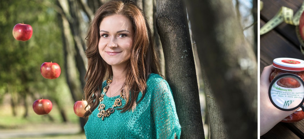 Uśmiechnięta kobieta w turkusowej bluzce i drewnianym naszyjniku, z jabłkami unoszącymi się wokół niej na tle drzew. Z prawej strony słoik dżemu jabłkowego, którego etykieta jest powiększona przez...