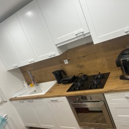 Kacper Markuszewski - Nowoczesna kuchnia z białymi szafkami, drewnianym blatem i czarną płytą grzewczą oraz piekarnikiem Hotpoint Ariston