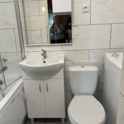 Kacper Markuszewski - Nowoczesna, biała łazienka z marmurowymi płytkami, umywalką z szafką, toaletą i pralką, widoczna instalacja elektryczna na ścianie.